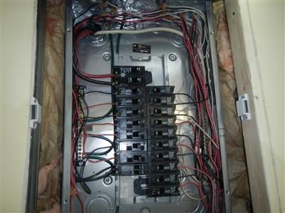 Open electrical panel with two columns of breakers and red, black and white wiring against pink insulation.