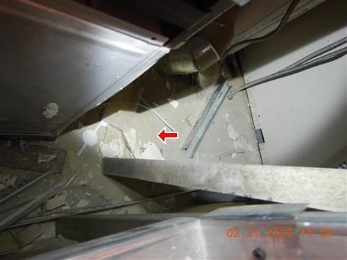 Looking down into a ceiling access opening with plaster dust and debris around an evaporator housing, red arrow on the debris.