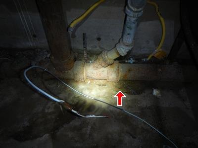 Corroded cast iron drain pipe near a basement floor with red arrow at a pipe joint