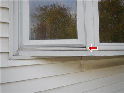 Vinyl window sill edge over horizontal siding with a red arrow at a gap in the trim