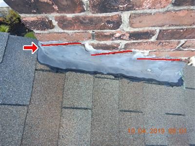 Grey lead flashing at the base of a brick chimney on a shingle roof with red lines marking cracks and a red arrow.