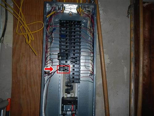 Open electrical panel with two columns of breakers, a red box and arrow marking one breaker on the left side.