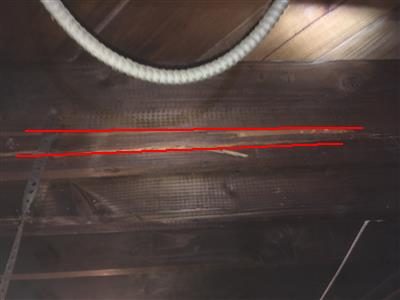 Underside of a wooden floor joist with a long split outlined by two red lines, a white pipe above it.