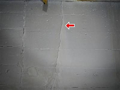 Grey concrete block foundation wall with a vertical crack running down it and a red arrow pointing at the crack.