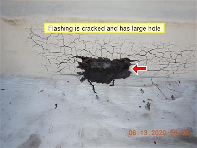 Cracked black flashing cement with a dark hole, labelled by the report and marked with a red arrow.
