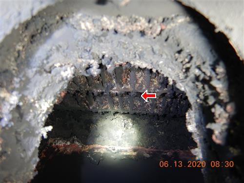 Looking into an open boiler with heat passages heavily coated in black soot, a red arrow pointing at the clogged galleys.