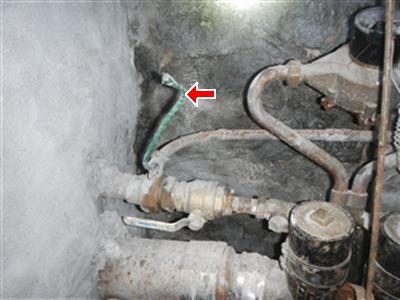 Green ground wire running loose beside a basement water main and meter, with a red arrow pointing at the wire.
