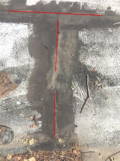 Flat roof surface with a T-shaped seam of dark roofing cement traced in red lines, and two round vents at the left edge.