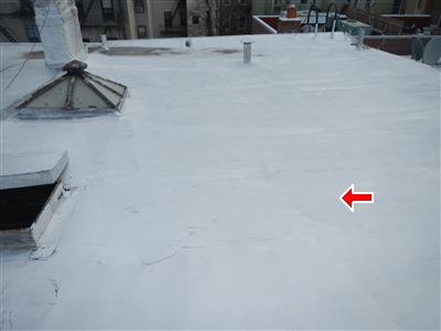 Silver-coated flat roof with a skylight curb and vent pipe, red arrow at a seam line