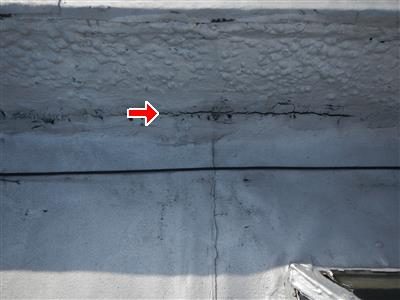 Light grey flat roof surface meeting a wall with a dark seam line and a red arrow marking surface cracking.