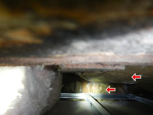 View through a small attic opening showing insulation pressed between rafters above a metal frame, two red arrows.