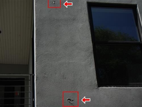 Grey stucco wall beside a tall window with two small holes marked by red boxes and arrows.