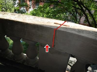 Stone balcony rail with balusters, a red line tracing a gap at a joint and a red arrow pointing up at it.