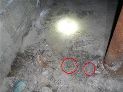 Dirt basement floor with two red circles around pipe fittings next to a cast iron drain line.