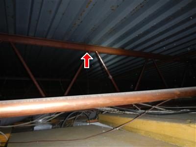 Steel bar joists and a copper pipe beneath a corrugated metal roof deck, red arrow on the joist.