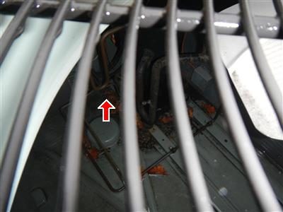 Looking through the grille of a rooftop air conditioning unit at leaves and debris around the coils, red arrow.