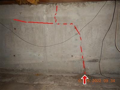 Poured concrete foundation wall with a long crack traced by red dashed lines and a red arrow at the floor.