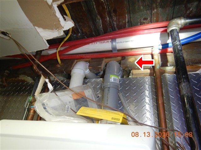Basement ceiling above a boiler with an opened ceiling, red and blue pipes and a red arrow pointing at a cut joist.