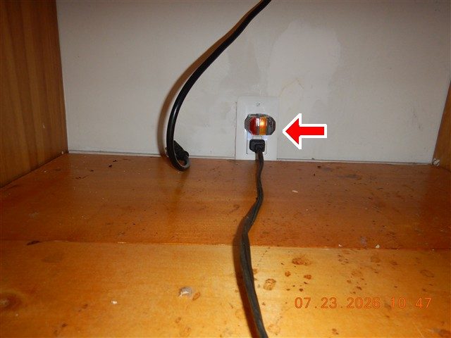 Outlet inside an empty dishwasher pocket under a counter with an orange plug-in tester, marked with a red arrow.