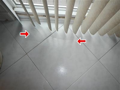 White ceramic floor tiles below vertical blinds with two red arrows pointing to cracks.