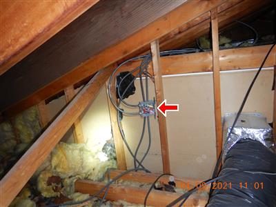 Attic framing and insulation with an open electrical junction box on a stud, marked by a red arrow.