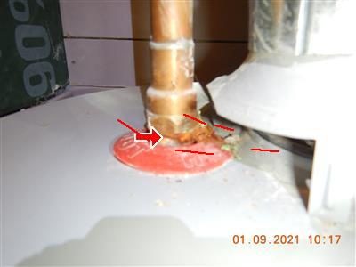 Close-up of a copper pipe and nipple at the top of a water heater with corrosion at the joint, marked by red arrows.