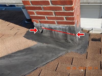 Brick chimney base on an asphalt shingle roof with a red line and arrows along the cracked flashing seam.