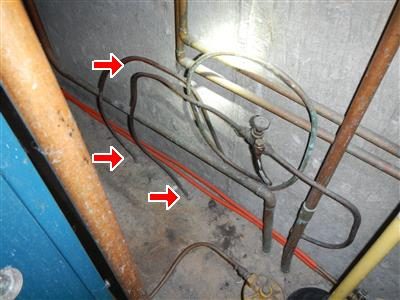 Basement floor by a boiler with three red arrows pointing at old copper lines rising out of the concrete.