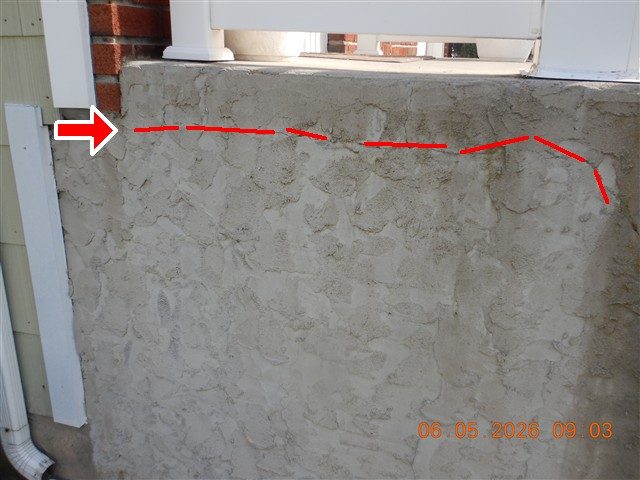 Stuccoed concrete stoop cheek wall with a horizontal crack traced by a red dashed line and a red arrow at the left.