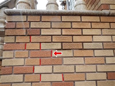 Tan brick stoop wall with several vertical mortar joints marked in red and a red arrow pointing at one joint.