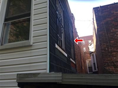 Rear extension wall with dark brick-pattern siding beside white vinyl siding, marked with a red arrow.