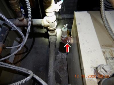 Boiler piping with a heavily corroded brass elbow fitting, marked by a red arrow.