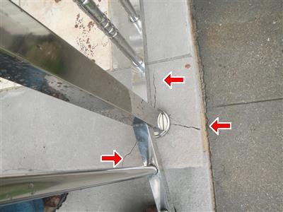 Stone stoop tread beside metal railing posts, with three red arrows pointing at cracks around the post base.