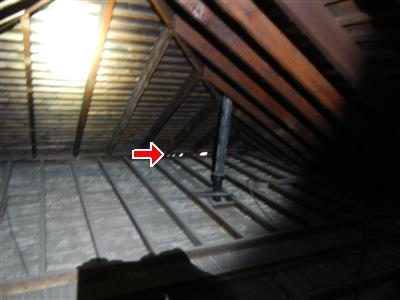 Dim attic with a steel post and wood rafters; a red arrow points at daylight showing through near the eave.
