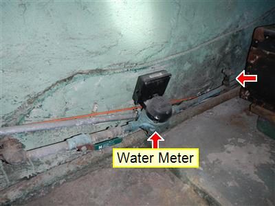 Basement water meter on a supply pipe along a green-painted wall, labelled 