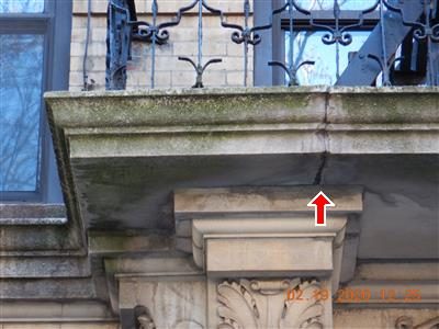 Carved limestone slab over a building entrance with a vertical crack above a decorative capital and a red arrow pointing up at it.