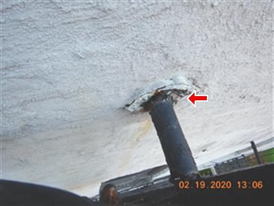 Rusted metal bracket where a roof ladder meets a stucco wall, with a red arrow pointing at the anchor.