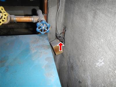Electrical outlet box hanging loose from a concrete wall beside a blue water valve, marked with a red arrow.