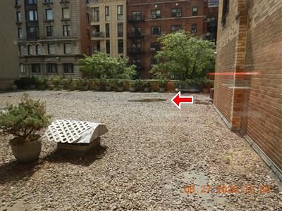 Gravel-covered roof over a garage with a wet patch at the drain, red arrow pointing at it, apartment buildings beyond.