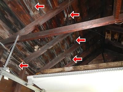 Underside of a garage roof with dark stained wood sheathing between rafters, marked by five red arrows.