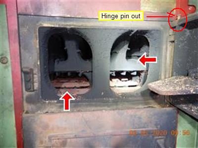 Open boiler door showing two sooty firebox chambers, three red arrows and a label reading hinge pin out.