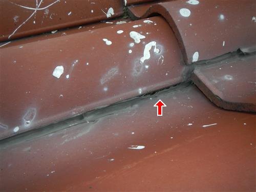 Terracotta clay roof tiles at a ridge, with a mortar patch seam arrowed.