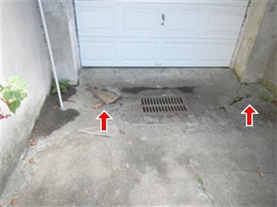 Floor drain grate in cracked concrete apron in front of a white garage door