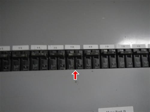 Row of breakers in a building electrical panel with unit labels above, a red arrow pointing to one breaker.