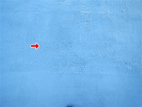 Pale blue painted flat roof surface with a network of fine cracks, a red arrow pointing at the crazed area.