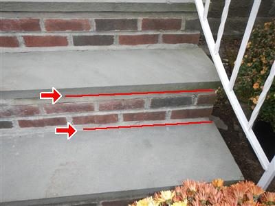 Brick and bluestone stoop steps beside a white railing, with red lines and arrows along two cracked mortar joints.