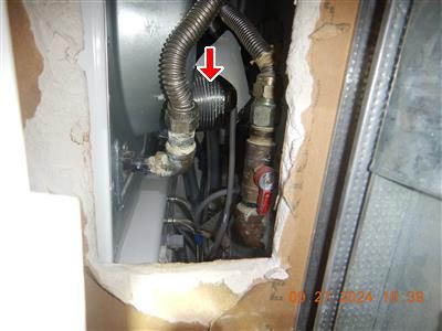 Flexible corrugated metal pipe and a shut-off valve behind an appliance, marked by a red arrow.