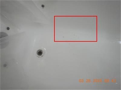 White bathtub floor near the drain with a red rectangle outlining small dark chips in the porcelain.