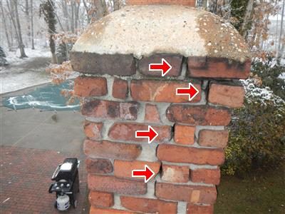 Brick boiler chimney with a concrete cap, four red arrows pointing at loose bricks and open joints.