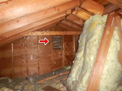 Attic gable end with a louvered vent between rafters and fibreglass insulation, red arrow at the vent.